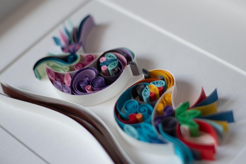 Picture of two handmade paper art birds in different vibrant colours of purples, blues, yellows, reds and greens. The birds are facing each suggesting closeness and friendship.