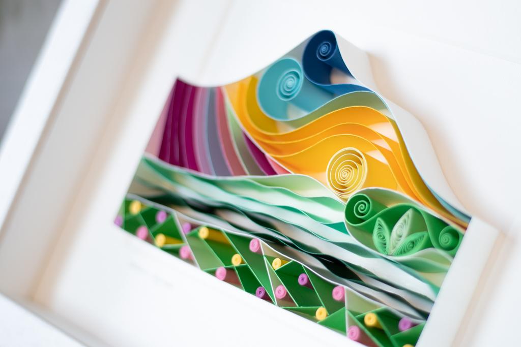 A zoomed in picture of a handmade paper art creation of Wicklow's sugarloaf mountain. Made of swirls of paper and on edge paper, the mountain is captured in a variety of colours including yellow, blue, green, purple and pink.