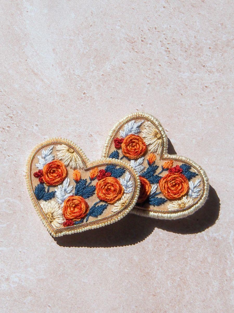 Broches brodées à la main en forme de cœur. Pièces limitées, finitions perles ou fil blanc, élégance artisanale en série limitée.