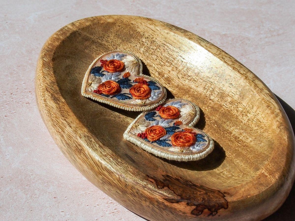 Broches brodées à la main en forme de cœur. Pièces limitées, finitions perles ou fil blanc, élégance artisanale en série limitée.