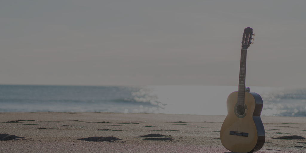 Une guitare sèche sur une plage de sable, avec la mer en fond.