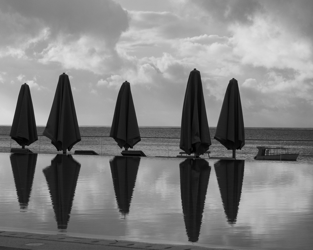 A black-and-white shot of an infinity pool reflecting closed beach umbrellas overlooking the Indian Ocean in Mombasa, Kenya.