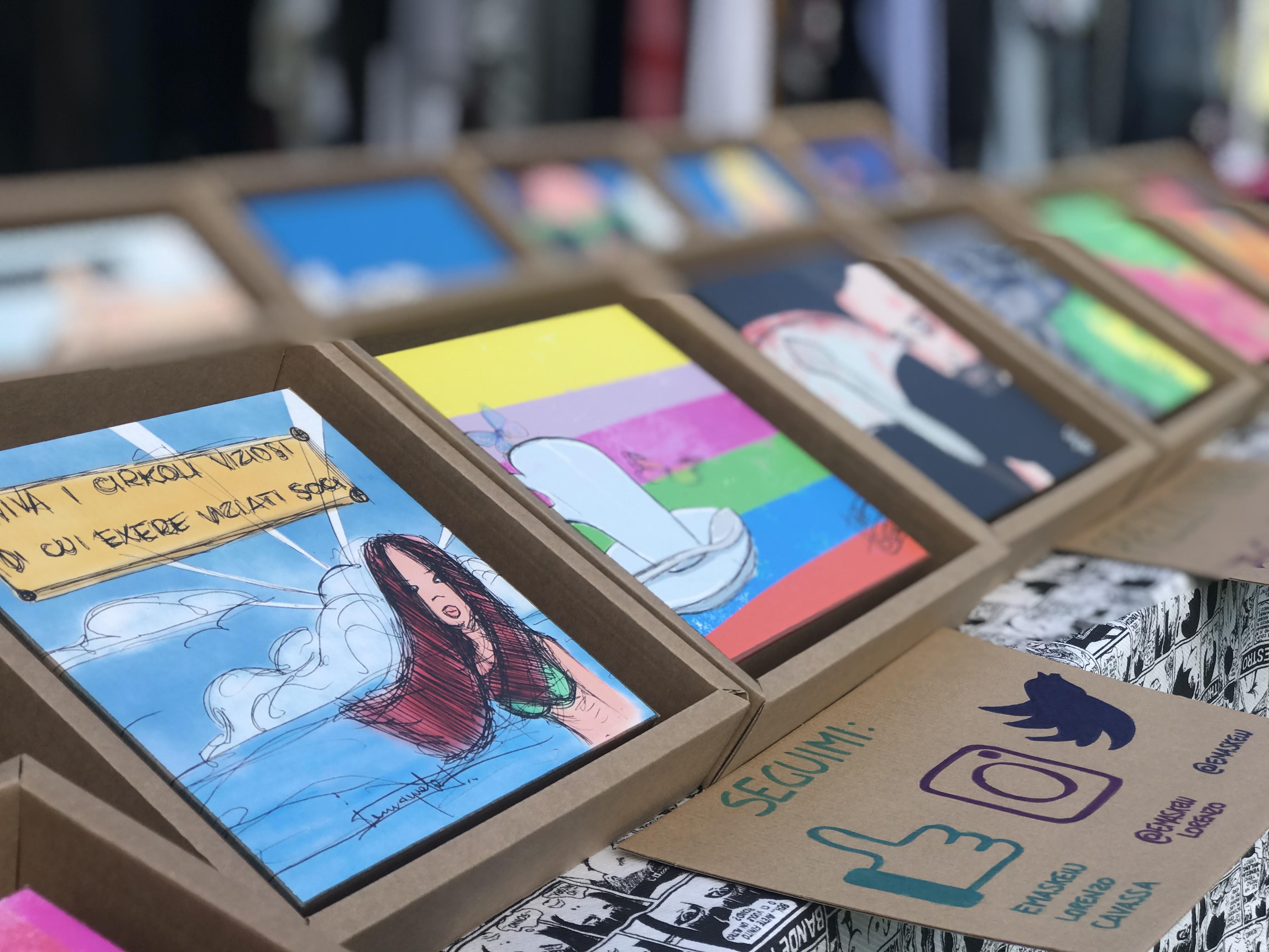 Illustrazioni stampate su cartoncino riciclato e disposte in esposizione su un tavolo.