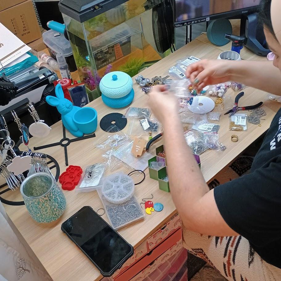 Person making jewelry at a desk with crafting tools and 3D prints