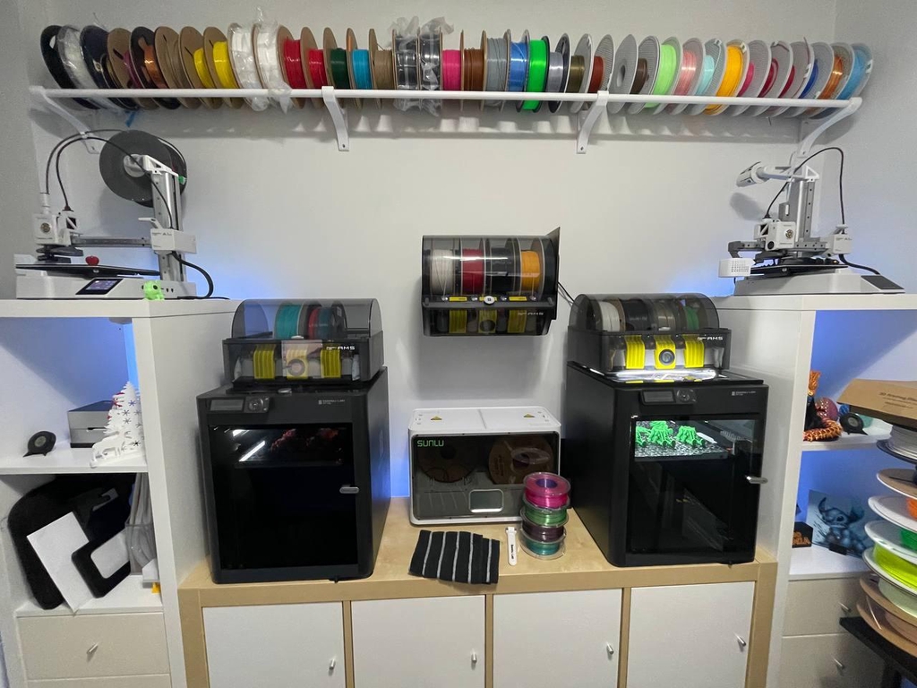 Organized 3D printing workstation featuring Bambu Lab X1 Carbon printers, AMS multi-filament system, colorful 3D printed figures, modeling tools, and efficient material storage in a home workshop.