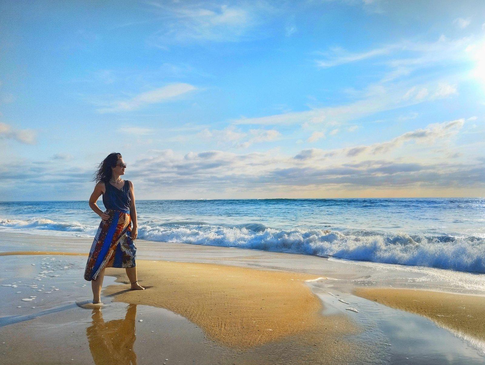 Alice, créatrice de la marque NJAXASS, en voyage sur une plage sauvage quelque part au bord de l'océan. Elle porte une jupe en patchwork de coton wax du Sénégal