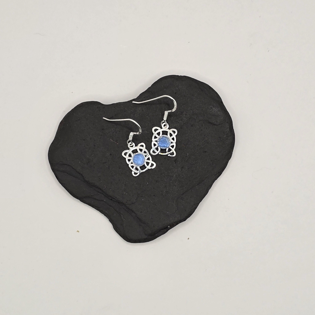 Handcrafted earrings featuring deep blue Scottish seaglass from Berwickshire beaches, set in silver-toned metal with an engraved floral and wave motif. The teardrop-shaped seaglass pieces are framed by a crescent-shaped base, combining natural coastal elements with intricate design. The earrings hang from simple silver hooks, offering a unique blend of beachcombed materials and artisan craftsmanship.