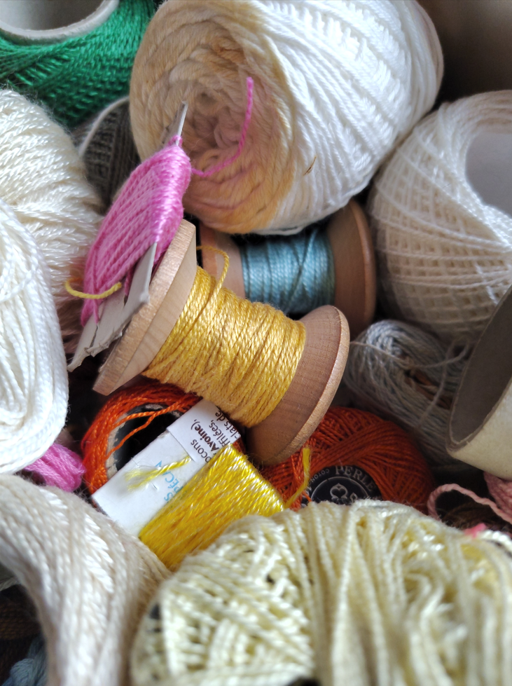 Boite remplie de bobines de fils à broder colorés.