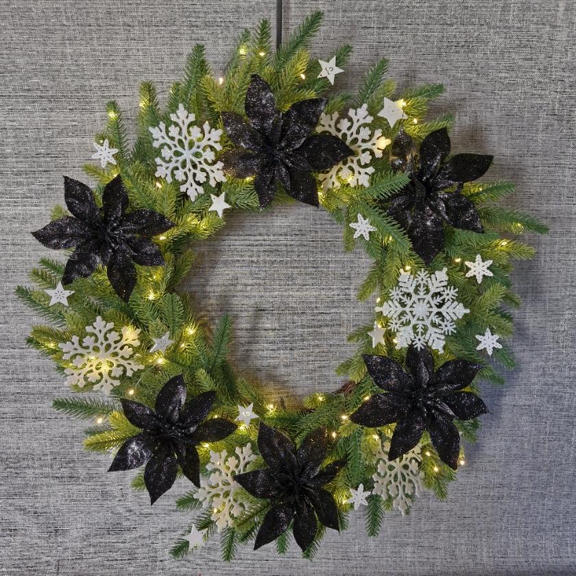 Artificial Christmas wreath with lights, black poinsettia flowers and white snowflakes