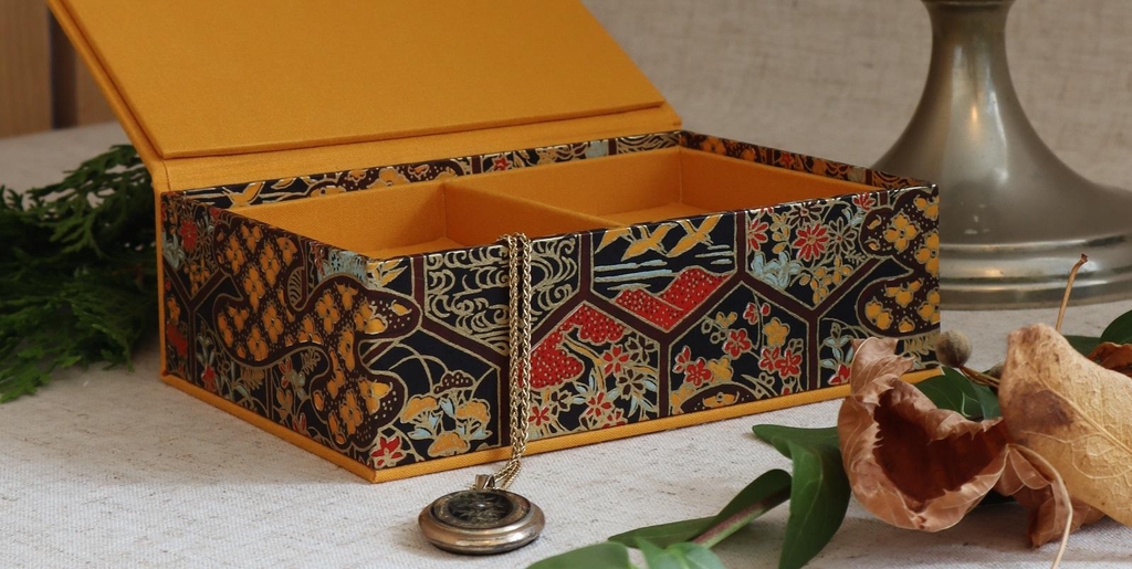 A handmade jewellery box in yellow hues serves as background to the main title 'Traditional Bookbinding' on the bookbinder homepage.