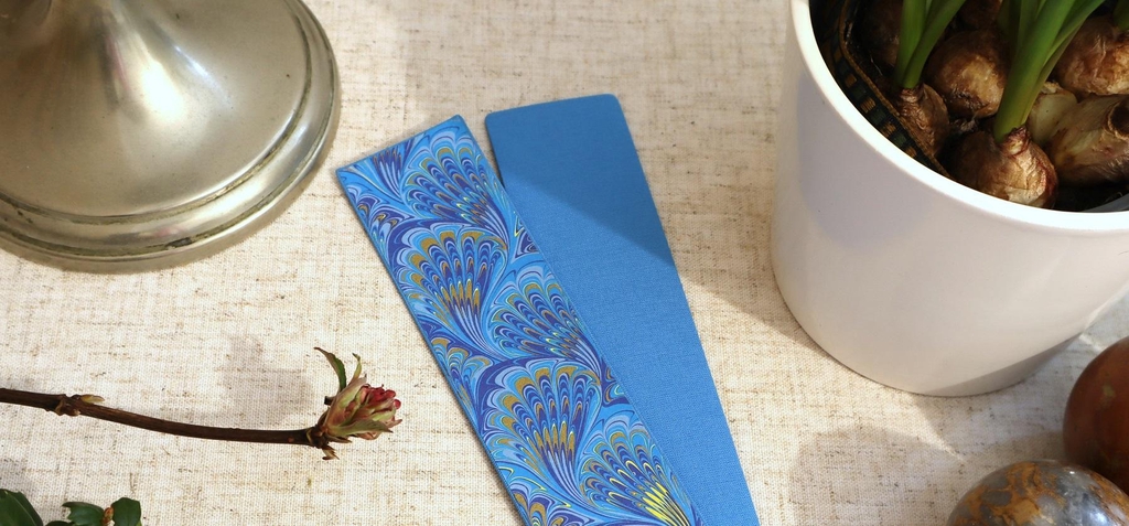 A handmade bookmark in sky blue cloth and Italian peacock marbling paper.