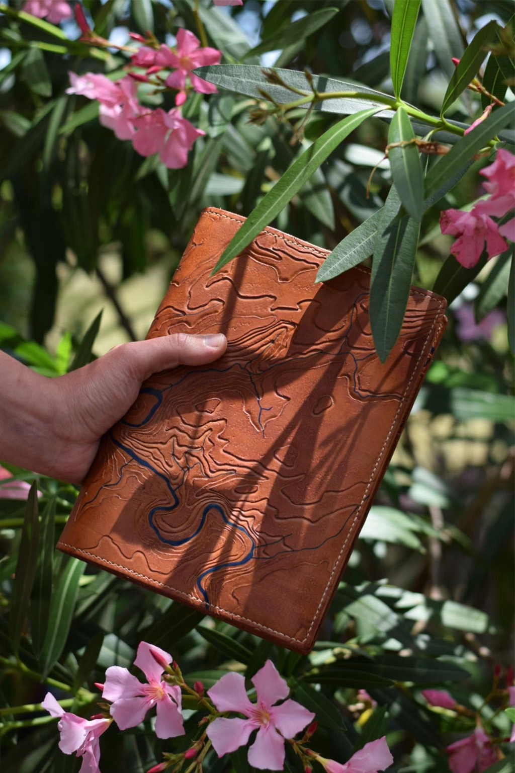 Photo d'un couvre-carnets en cuir de la marque Helix échappée cuir. Crée sur-mesure, il représente une carte topographique des gorges de l'Ardèche mise en relief par la technique du repoussage.