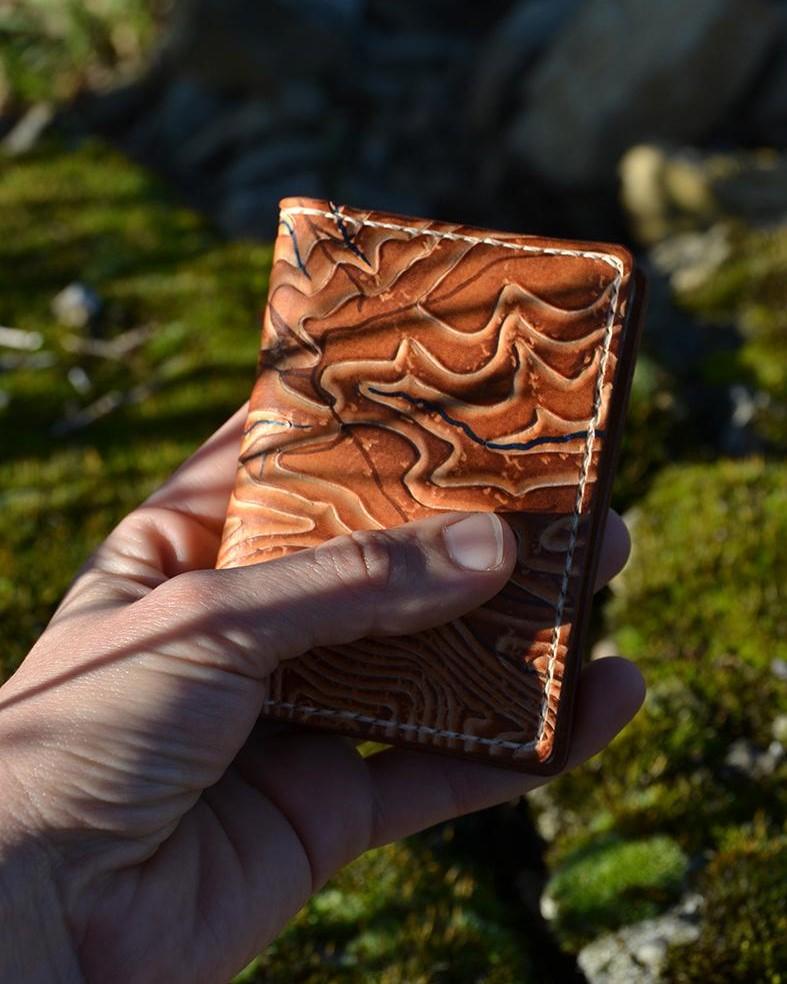 Photo d'un porte-cartes en cuir de la marque Helix échappée cuir. Crée sur-mesure, il représente un fragment de carte topographique des Pyrénées-Atlantiques mise en relief par la technique du repoussage.