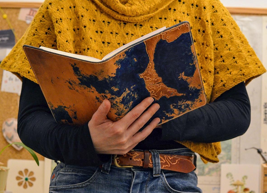 Photo d'un couvre-carnet en cuir de la marque Helix échappée cuir. Crée sur-mesure, il représente une carte de la presqu'île de Quiberon (Bretagne) mise en relief par la technique du repoussage.