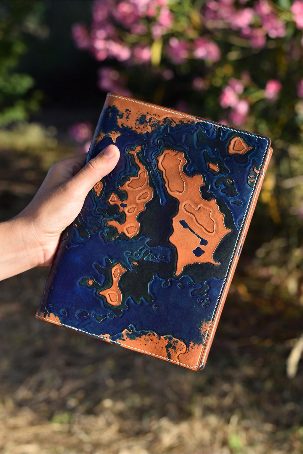 Photo d'un couvre-carnets en cuir de la marque Helix échappée cuir. Crée sur-mesure, il représente une carte topographique des îles Scilly (Angleterre) mise en relief par la technique du repoussage.