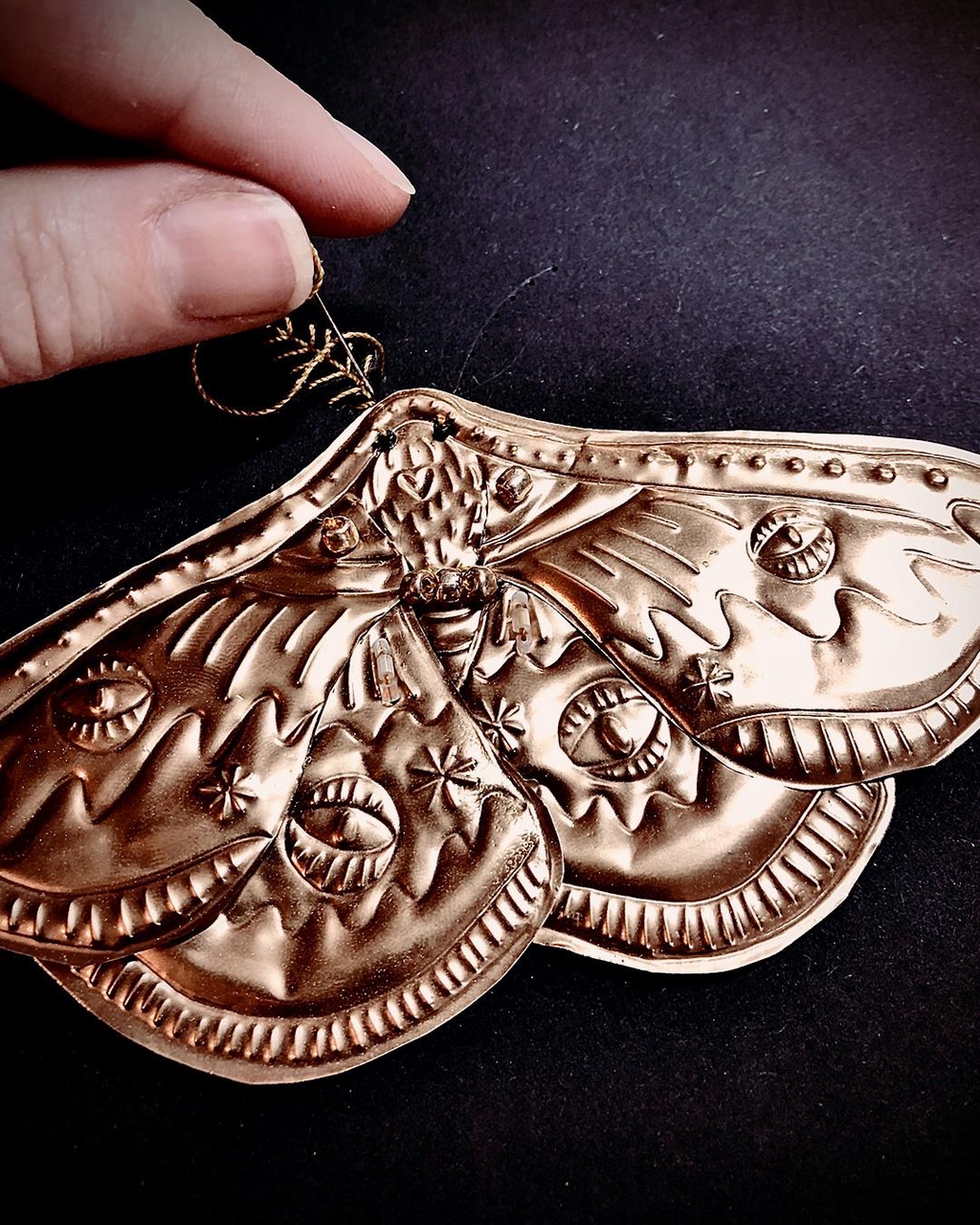 photo de l'artisan entrain de broder les antennes d'un papillon en métal embossé.