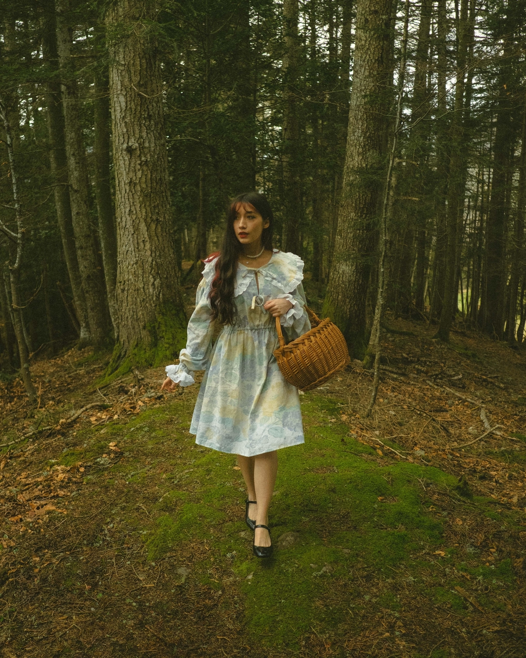 Jeune femme brune portant une robe aux couleurs pastel à volants et un panier, marchant dans la forêt