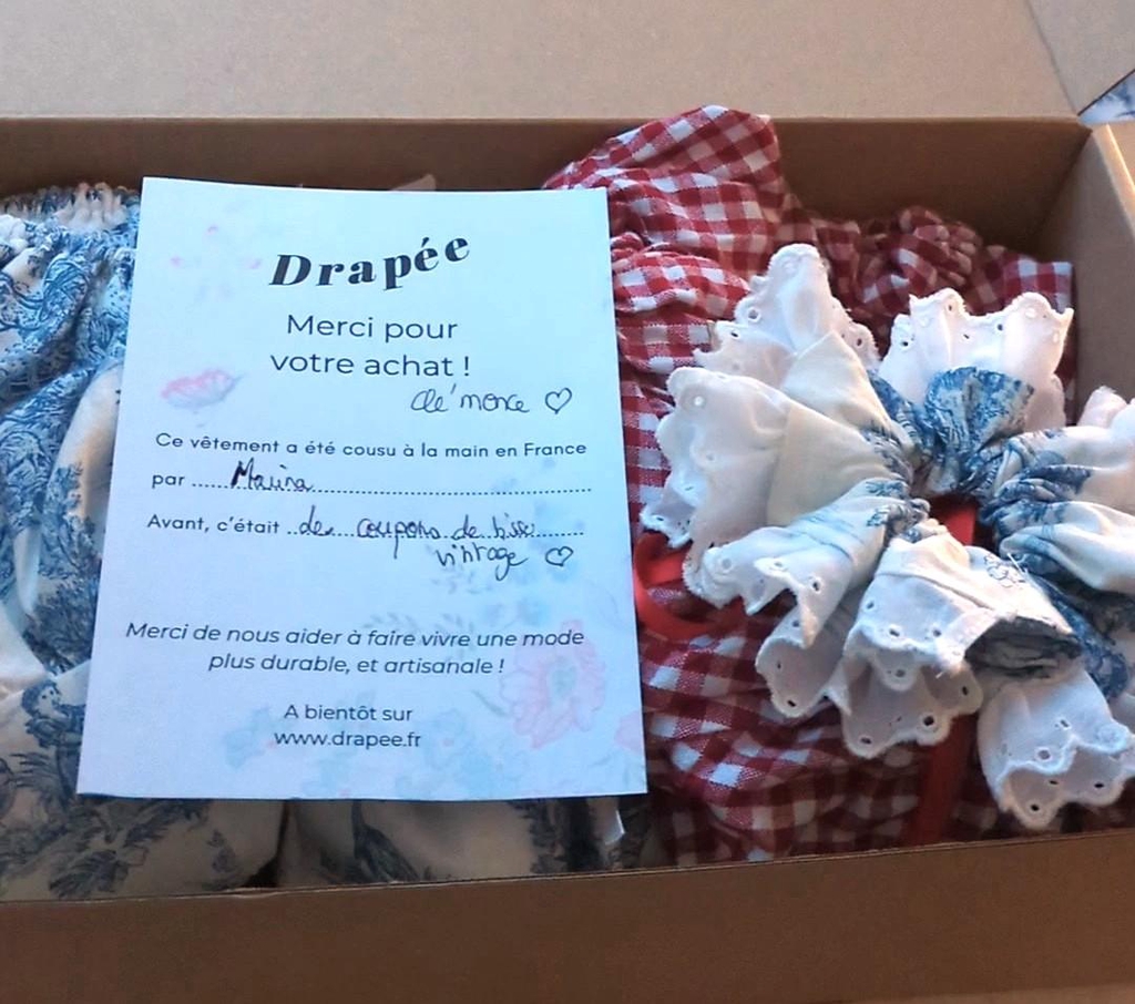 Boîte en carton d'expédition contenant une carte de remerciement à l'attention d'une cliente ainsi que deux vêtements et un chouchou