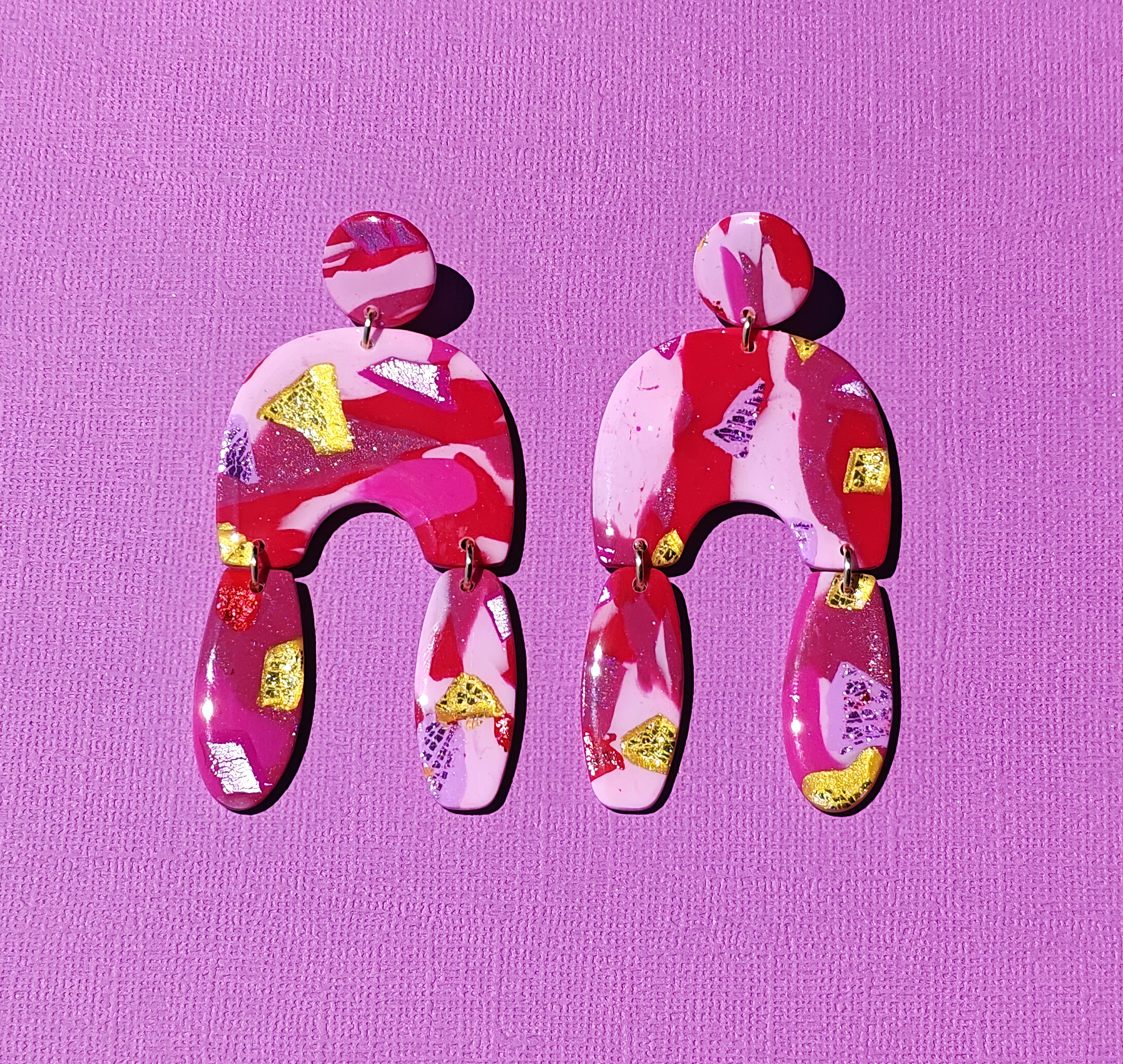 Handgemaakte statement oorbellen uit de Viva collectie van Miel-oorbellen, in roze, rood en fuchsia met glanzende gouden en metallic accenten.