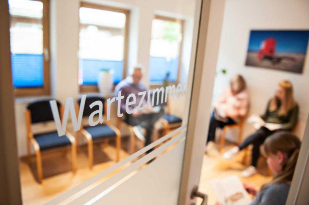Eine geöffnete Tür zm Wartezimmer, Patientn sitzen und lesen in einer Zeitschrift