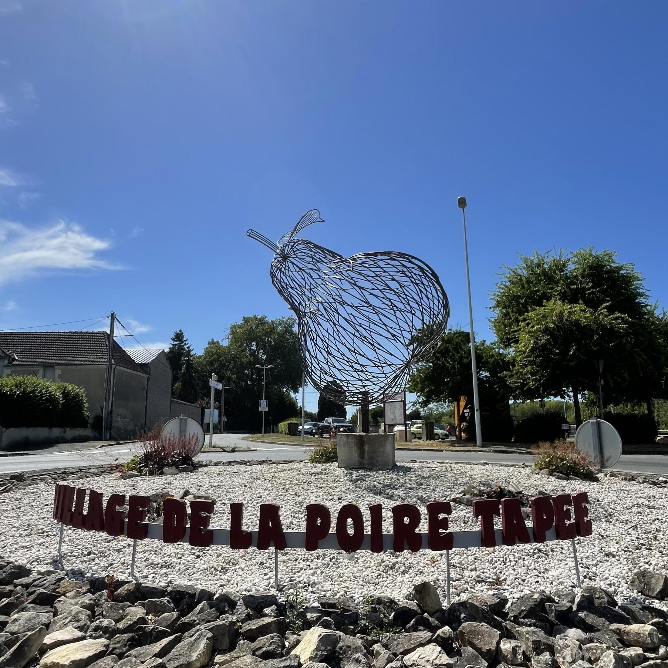 Cette sculpture de 3 mètres en métal rouillé, installée au rond-point central de Rivarennes en Indre-et-Loire, représente une poire en hommage à la tradition de la poire tapée. Les tiges entrelacées symbolisent les liens sociaux et le partage des traditions locales, notamment la poire tapée, spécialité où une poire est insérée dans une bouteille d'eau-de-vie.