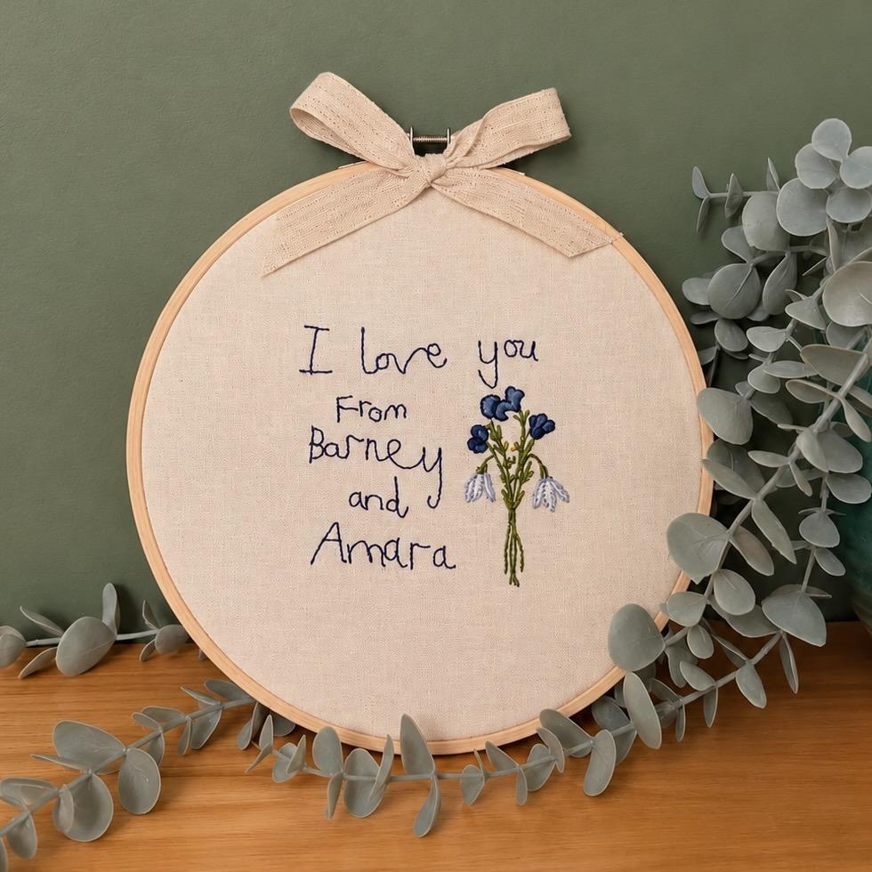 A child's handwriting embroidered on to a cream linen fabric and mounted in a wooden frame.