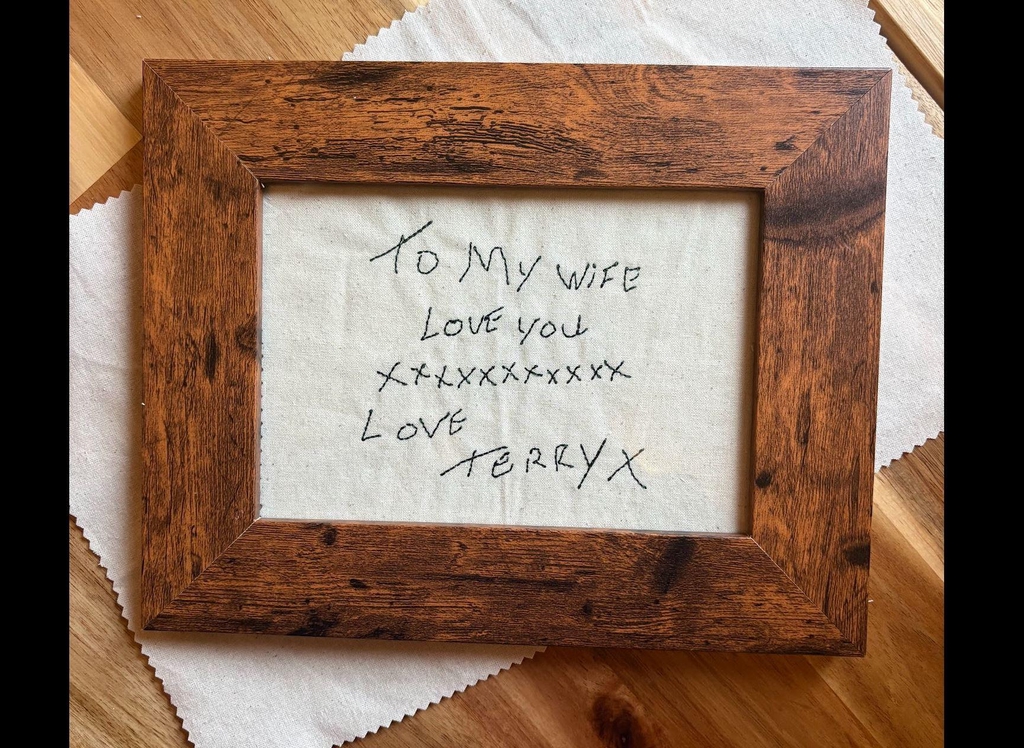 Handwriting embroidered on to cream linen fabric and framed in a dark wooden frame.