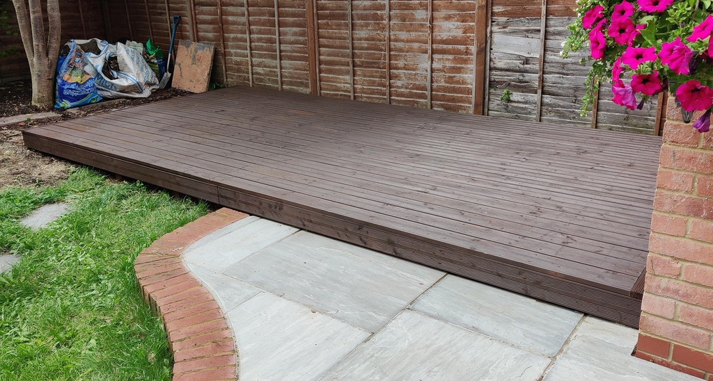 brown decking laid next to grey stone slabs and grass