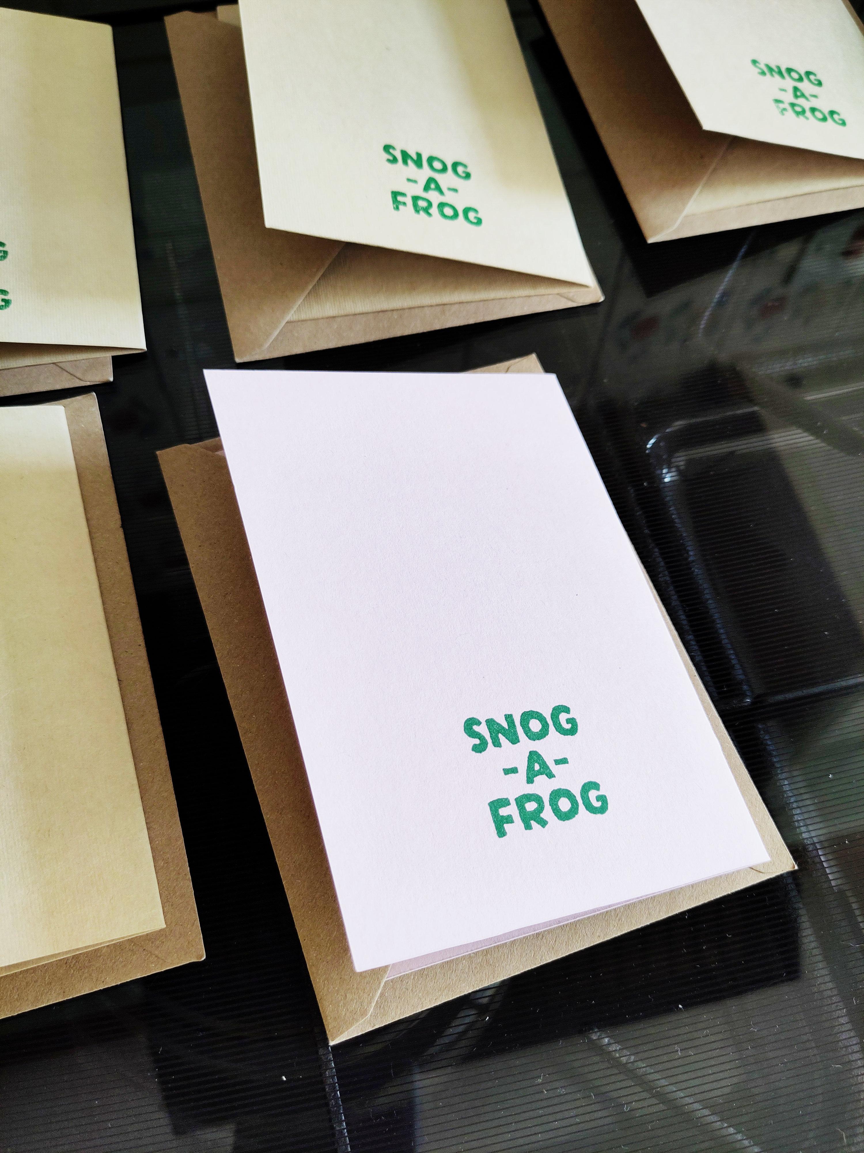A collection of cards lying face down with their envelopes. Each card has a green stamp on the back reading Snog-A-Frog.