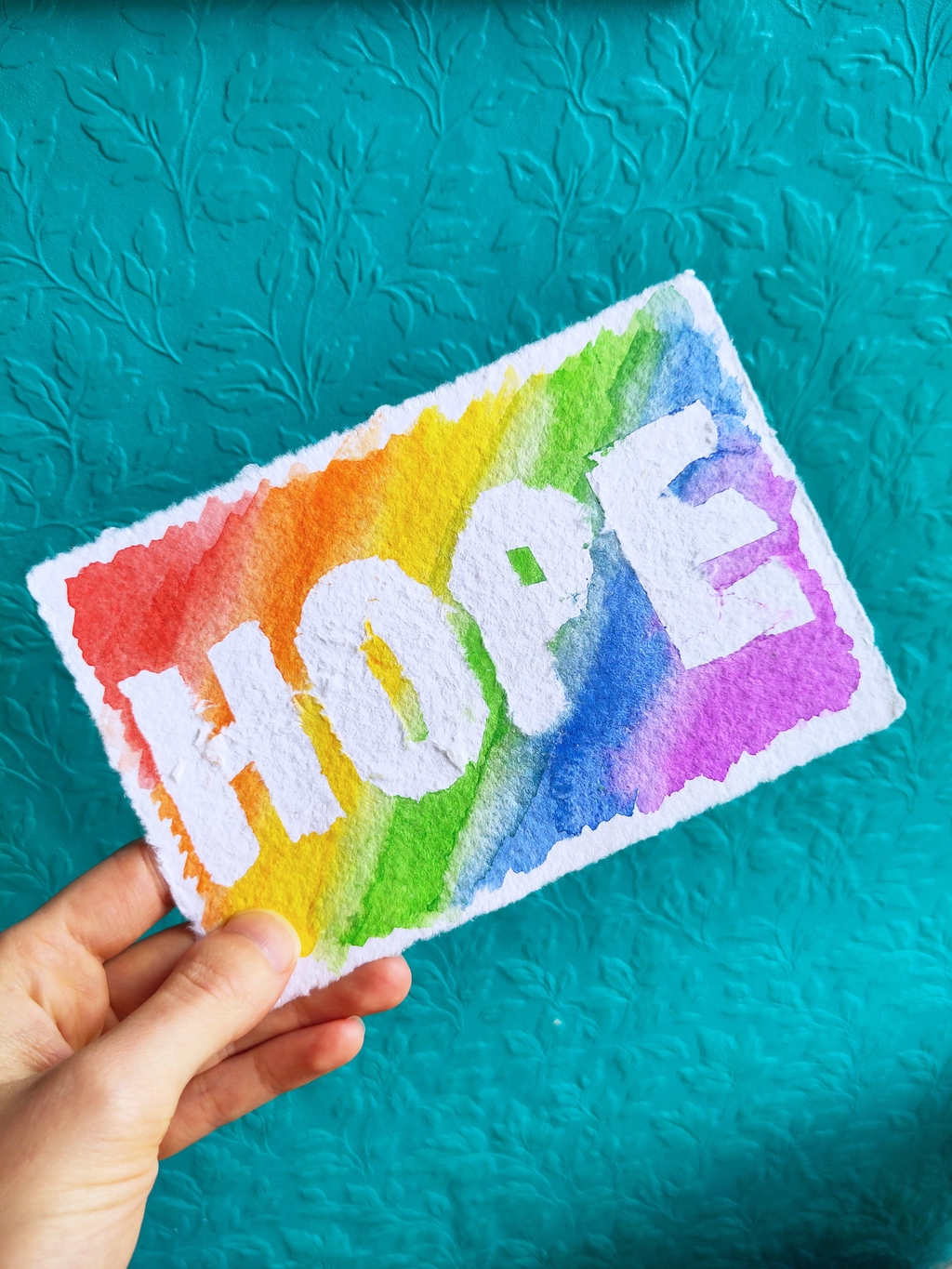 A watercolour rainbow with the word hope blanked out in white.