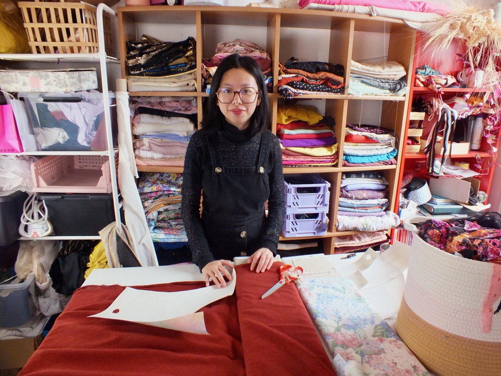 La créatrice rennaise dans son atelier, devant une étagère pleine de tissus, derrière la table de coupe.