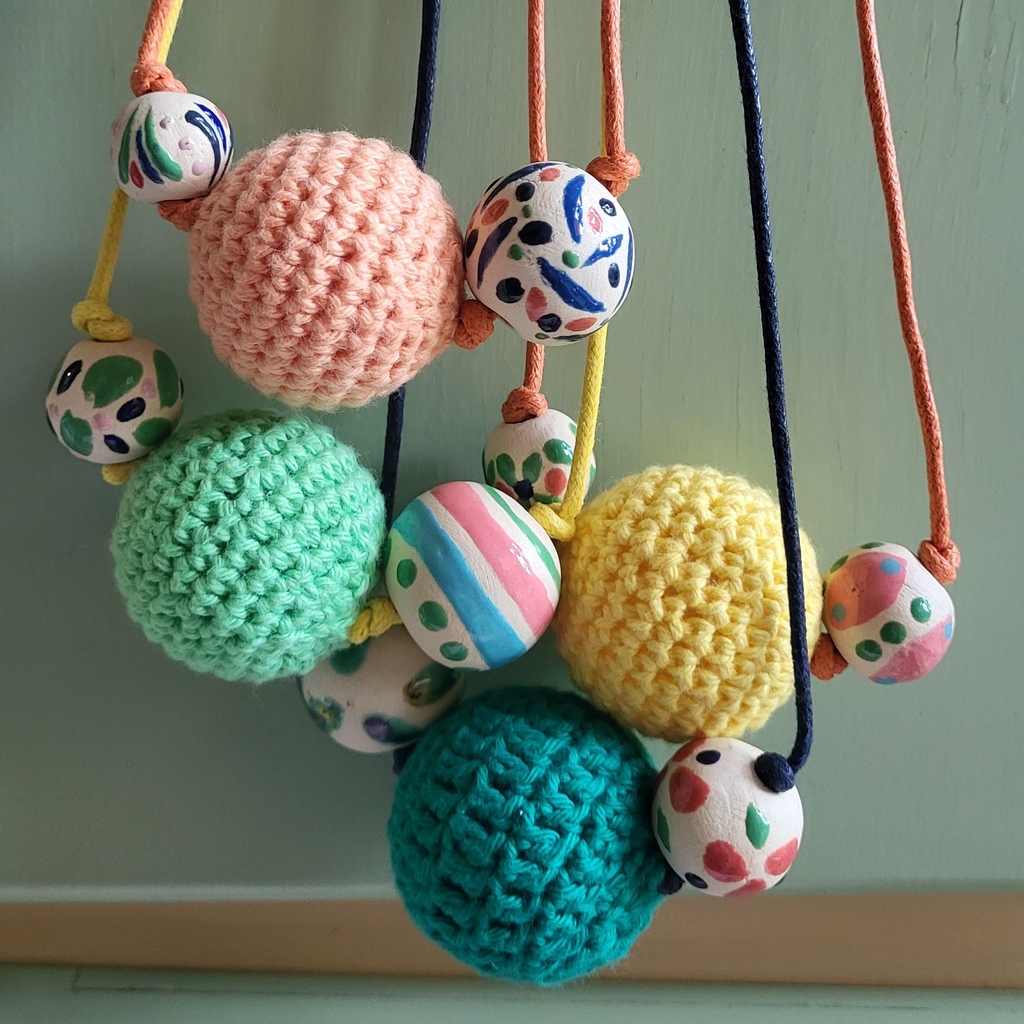 A hanging selection of pastel coloured necklaces made up of ceramic and crocheted beads.