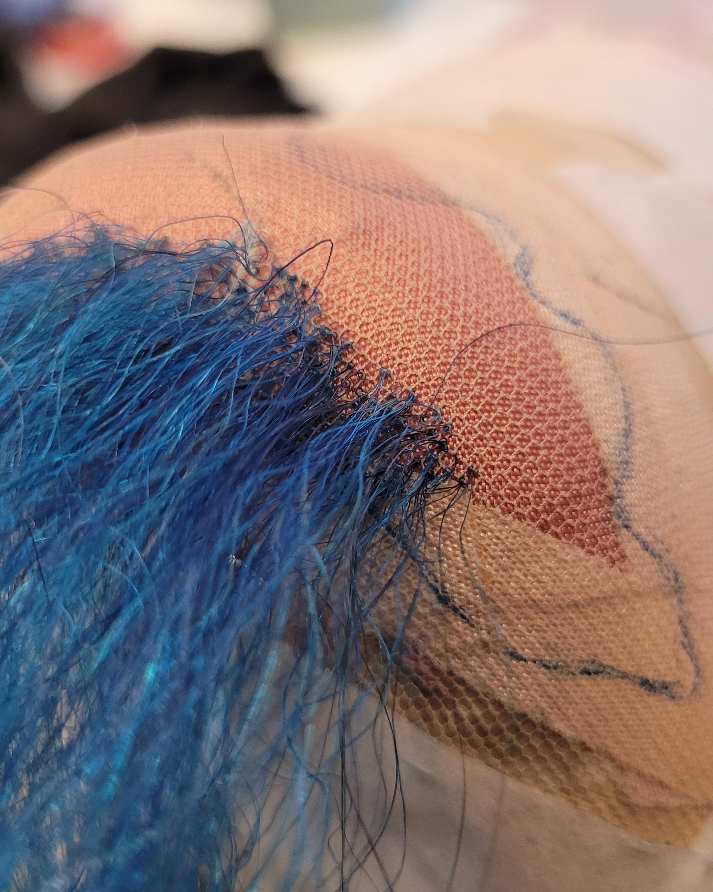 Detailaufnahme von den Knoten eines noch nicht fertig geknüpften Bartes mit blauen Haaren
