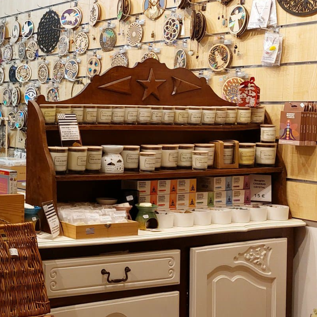 Présentation en boutique de produits bien‑être : bougies en bocaux, bougies chakra en boîtes colorées, brûleurs en céramique et petits accessoires exposés sur une étagère en bois, savons naturels et encens ecocert