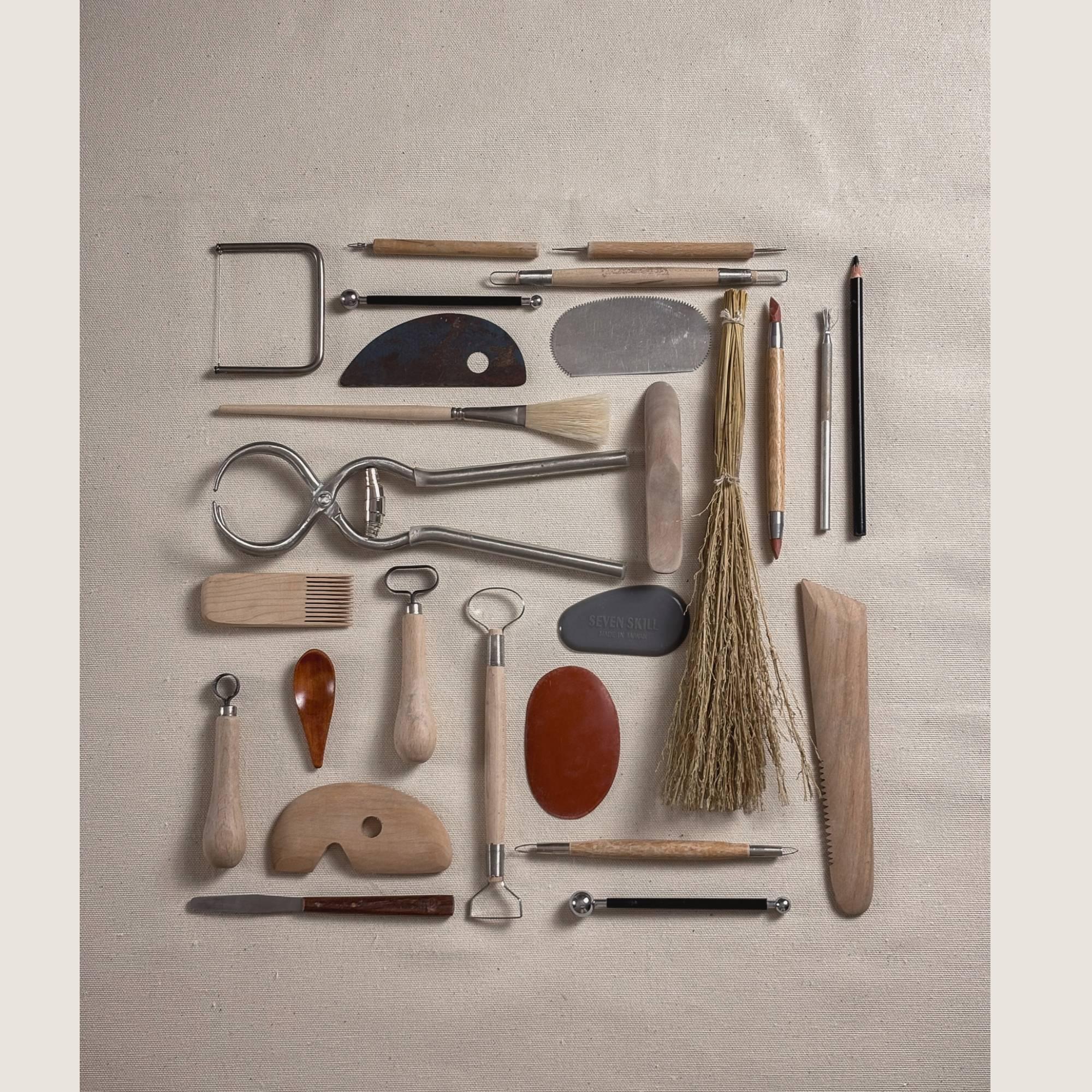 A curated flat lay of professional ceramic tools used by Rita Esteves: metal ribs, trimming loop tools, calipers, brushes, and wooden modeling tools on a linen background, representing the artisanal craft process.