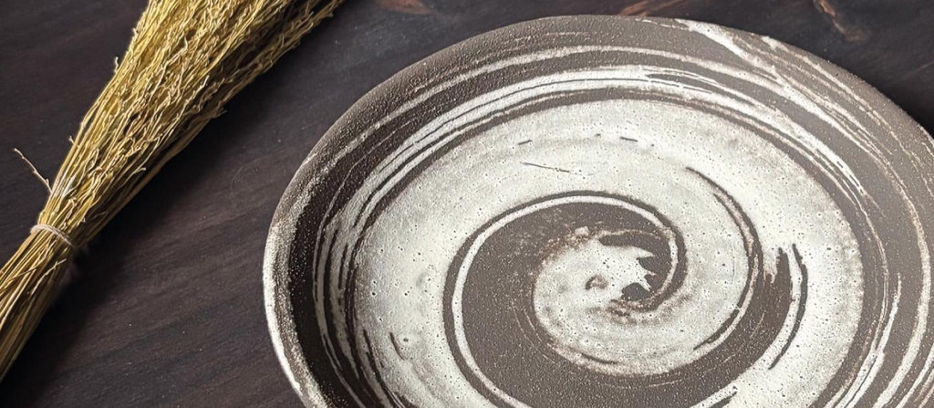 Close-up of a Rita Esteves Ceramics stoneware plate featuring a hand-painted brown and beige spiral texture, evoking natural earth patterns.