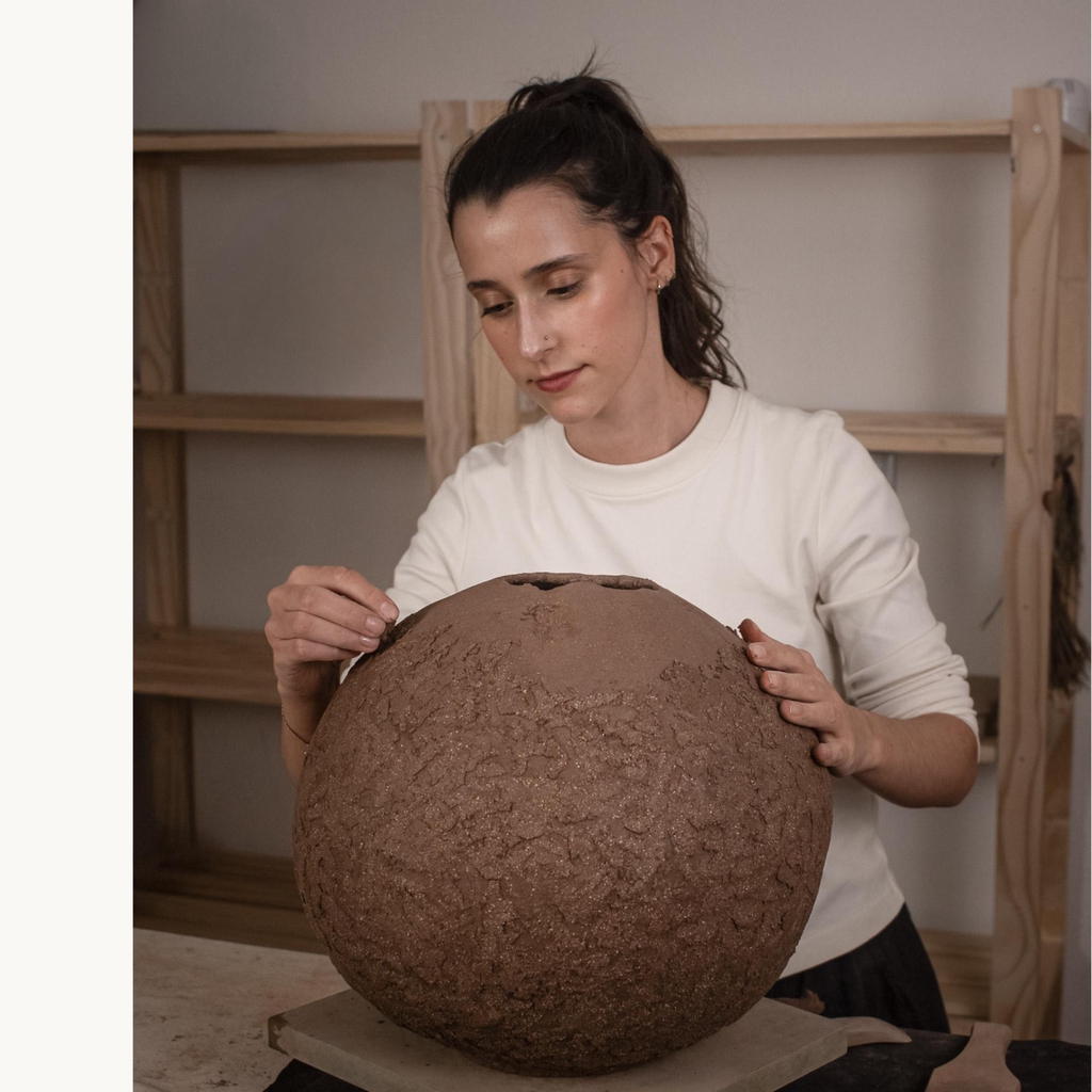 Ceramic artist Rita Esteves in her studio, hand-sculpting a large textured clay vessel, showcasing the slow, intentional process of Portuguese pottery.