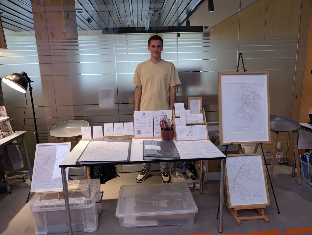 Verkaufsstand mit minimalistischen Stadtplan-Postern und Postkarten von Bielefeld, inklusive gerahmter Kunstdrucke und Preisliste.
