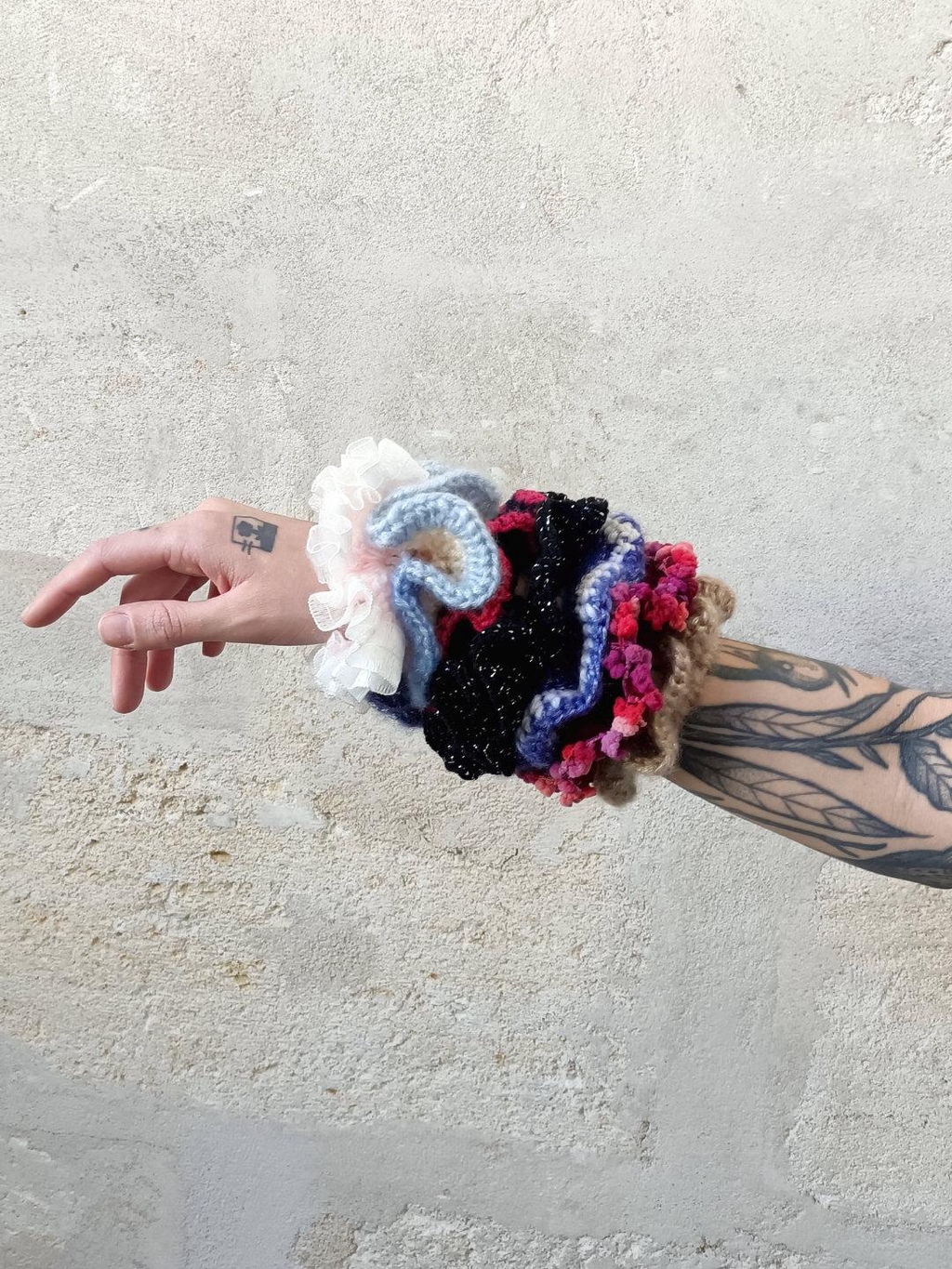 bras tatoué sur fond en pierre beige, sept chouchous en crochet multicolores sont enroulés autour du bras
