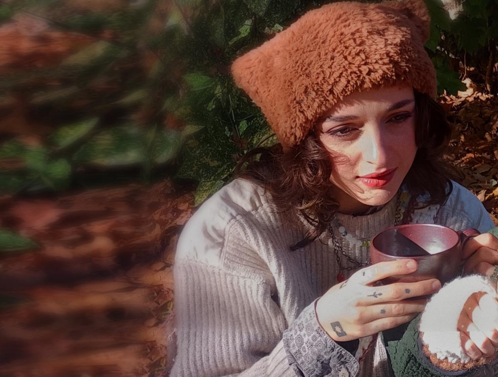 deux personnes portant des bonnets en fausse fourrure à oreille de chat buvant un café dans des tasses en grès dans un environnement naturel avec des arbres et feuilles mortes autour. Lumière chaleureuse et vive