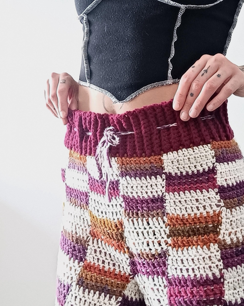 jeune femme portant un t shirt crop top noir aux coutures blanches et un short en crochet à motifs damier bordeaux et blanc