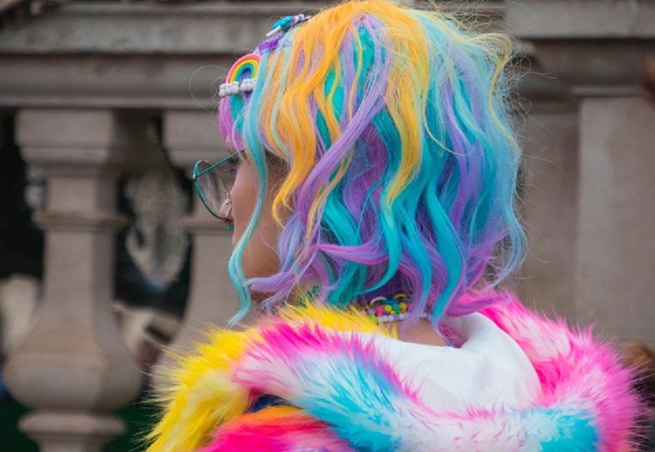 US Shipping information on a background of the back of a female with blue purple and yellow rainbow hair wearing a fluffy rainbow jacket