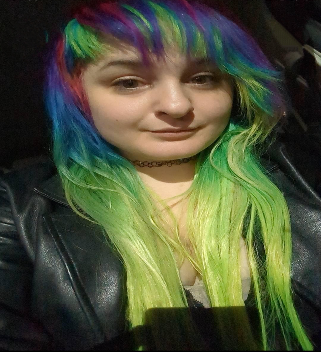 A photo of a customer wearing the wig she purchased from my shop, it's a mix of pink, purple, turquoise green and fluorescent yellow in a scene hair style 