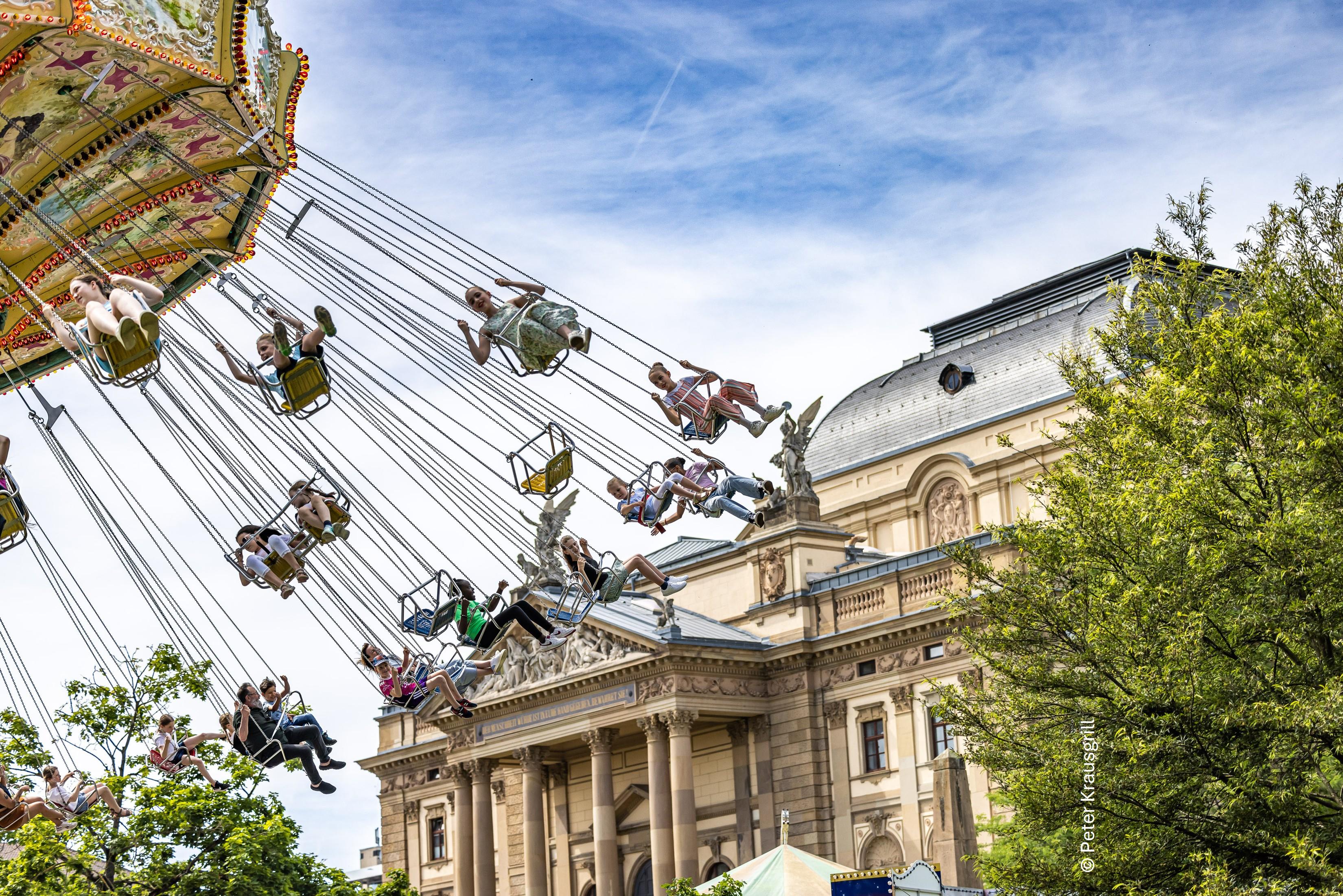 Menschen im Kettenkarussell fliegend vor der Rückseite des Wiesbadener Staatstheaters anlässlich des Wilhelmstraßenfests
