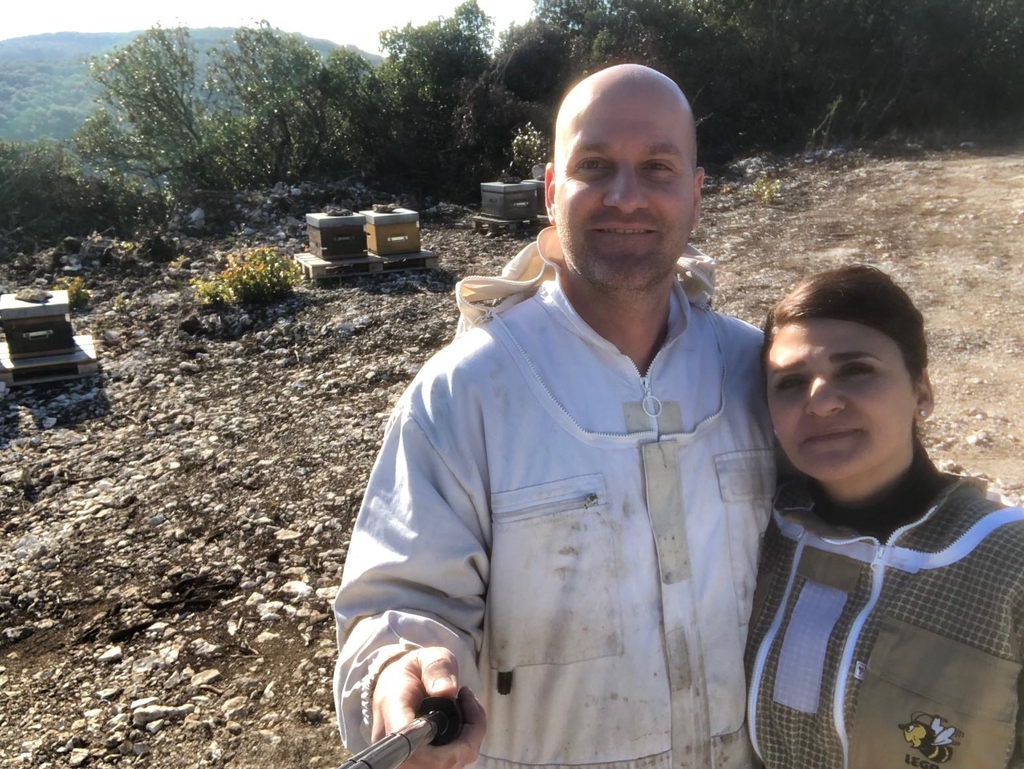 Un couple d'apiculteurs en tenue de travail sur leur terrain où sont posées les ruches.