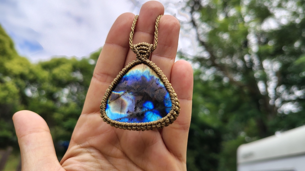 Labradorite irisée portée dans la main devant un paysage vert flou