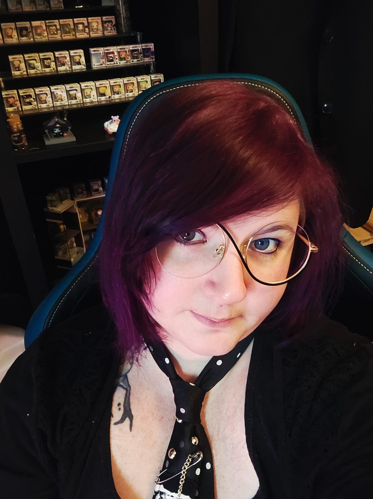 Junge Person mit dunklen Haare und asymmetrischer, runder Brille.
