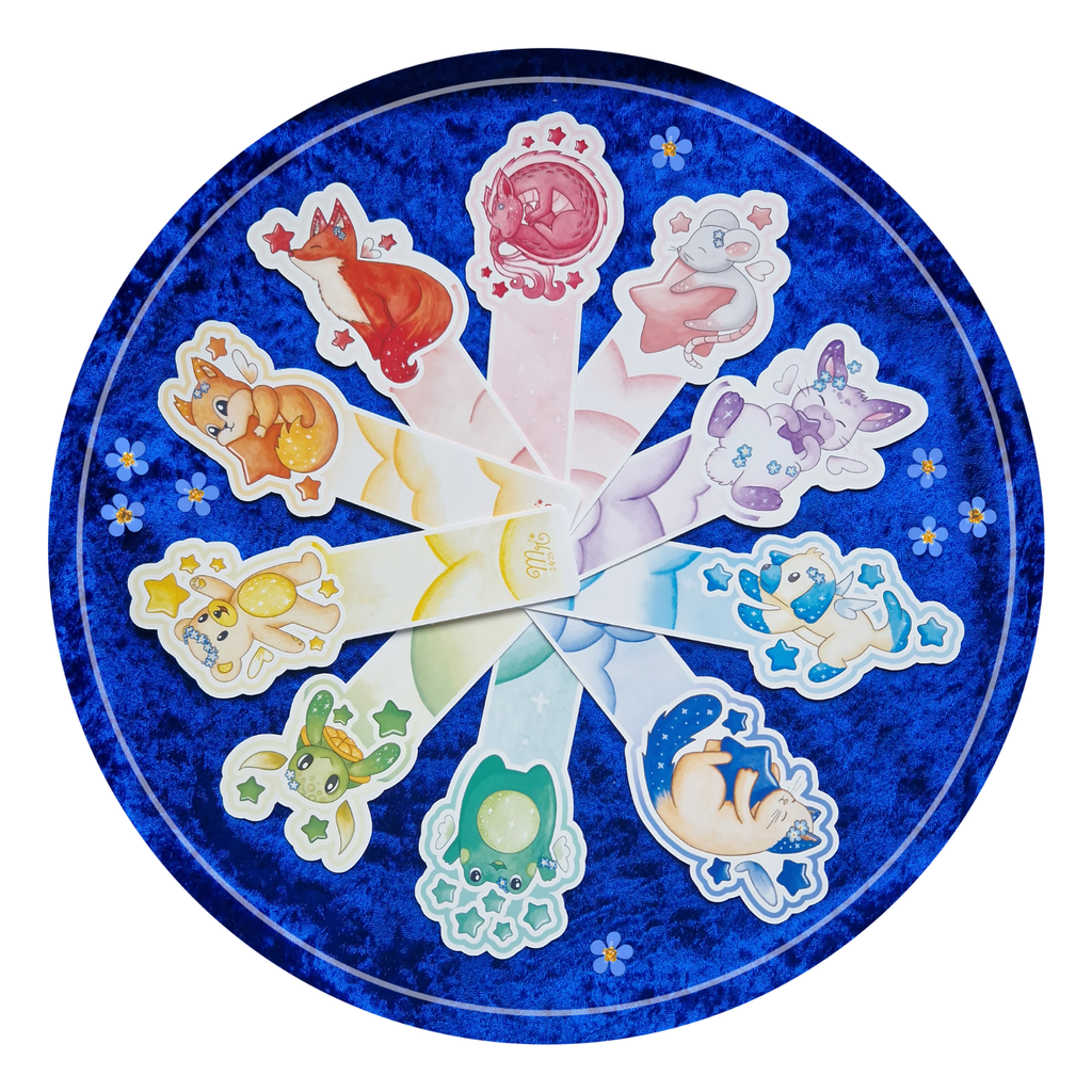 Zoom sur la collection stellaire de marque-pages de Mylarosy : positionnés en cercle par teinte donnant un effet arc-en-ciel sur fond bleu, parsemé de myosotis.