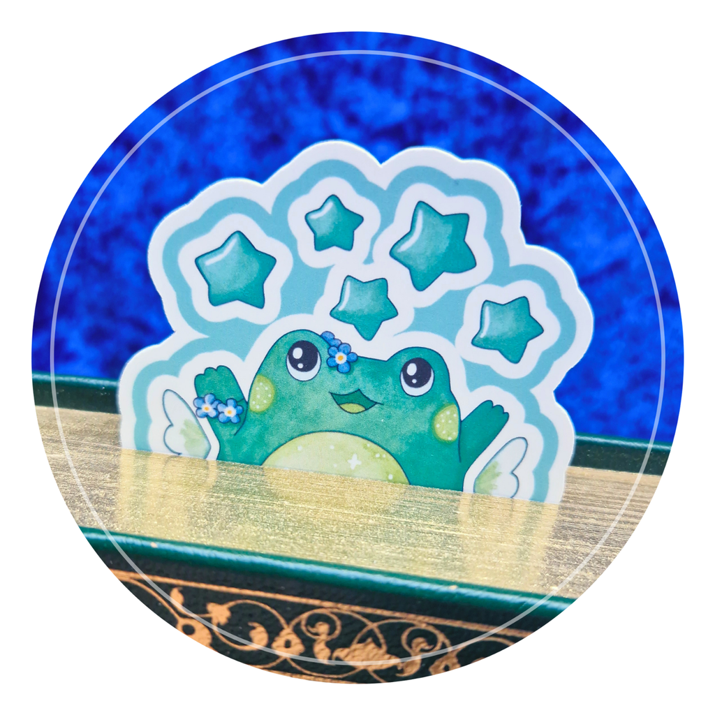 Zoom sur le marque-page grenouille stellaire qui dépasse d'un livre fermé dont la tranche est dorée.