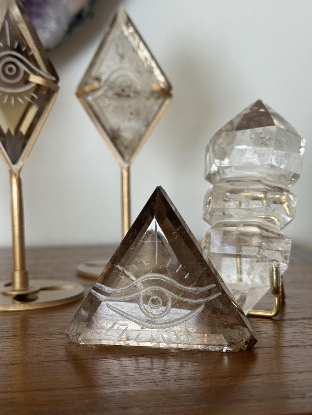 Quartz fumé sculpté en forme de losange, monté sur un socle doré élégant. Chaque pièce unique présente des inclusions naturelles et un symbole gravé d’un œil, ajoutant mystère et énergie protectrice. Parfait pour une décoration raffinée ou comme objet spirituel.